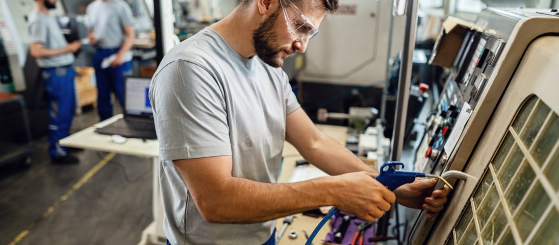 Young engineer operating a CNC machine in production line in a factory.